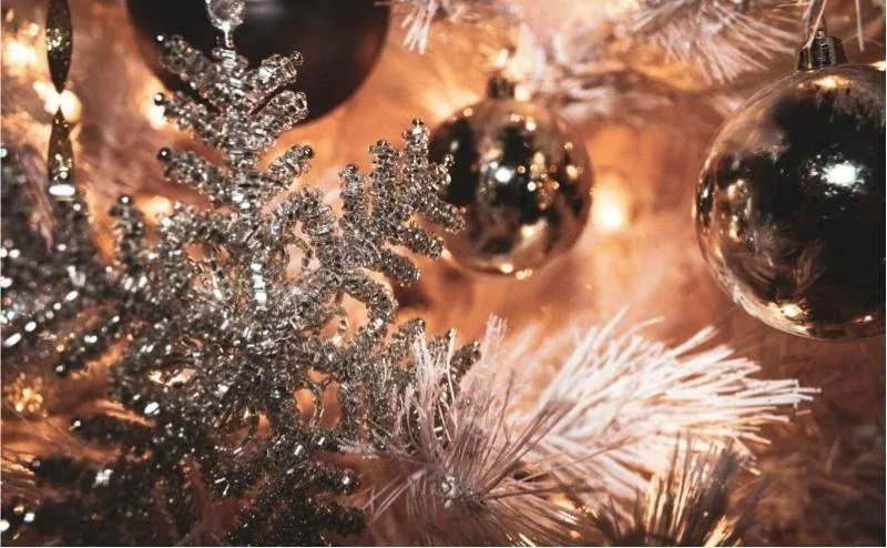 A silver glitter snowflake and reflective baubles displayed on a lit Christmas tree