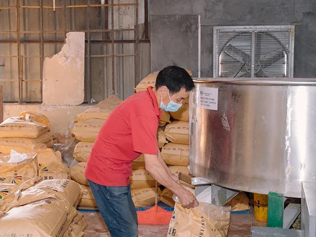 A XUCAI operator filling a bag of glitter at a production packing workstation