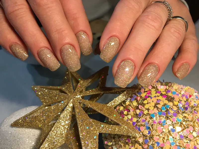 Hands with a gold glitter manicure resting above festive star decorations