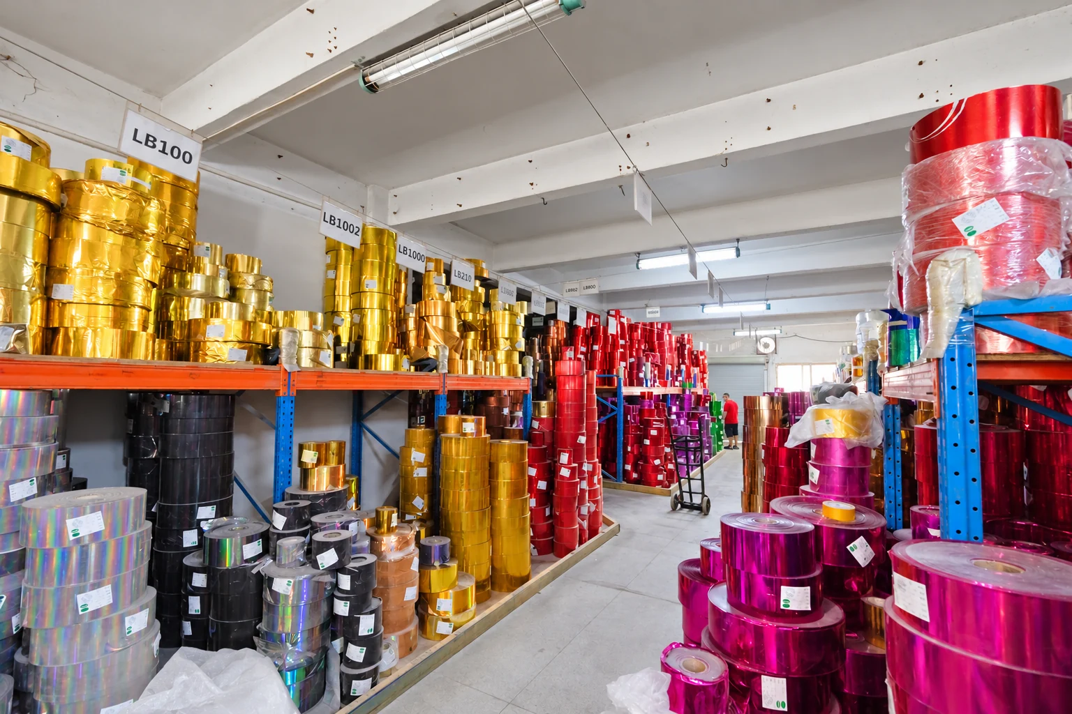 Gold, red, magenta and holographic film rolls stored on shelves at XUCAI